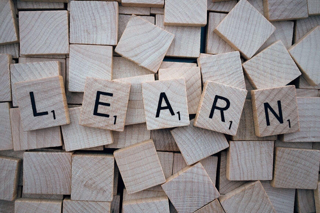 Wooden letter tiles arranged to spell learn on a background of scattered tiles.