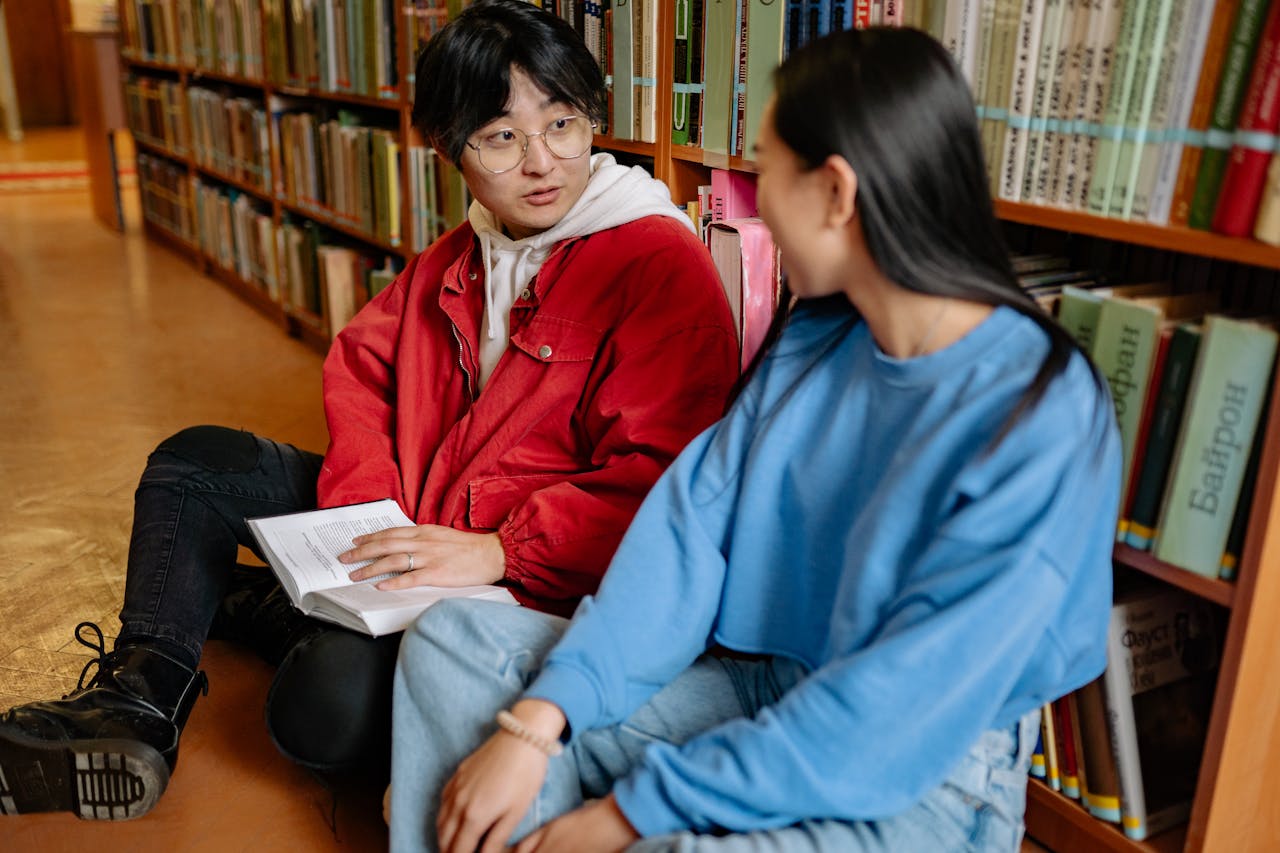 Two students sitting on the library floor, engaging in conversation and studying together.